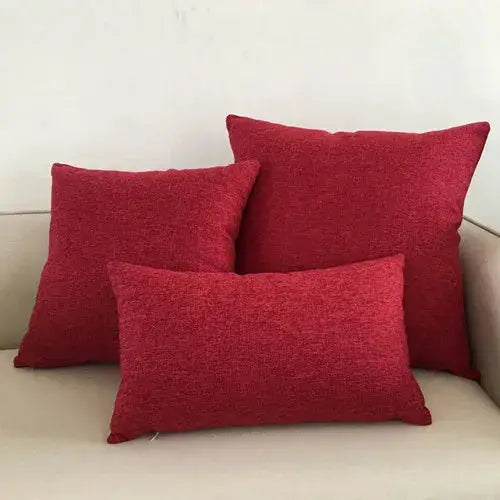 Three red decorative sofa cushions with textured fabric on a beige sofa.