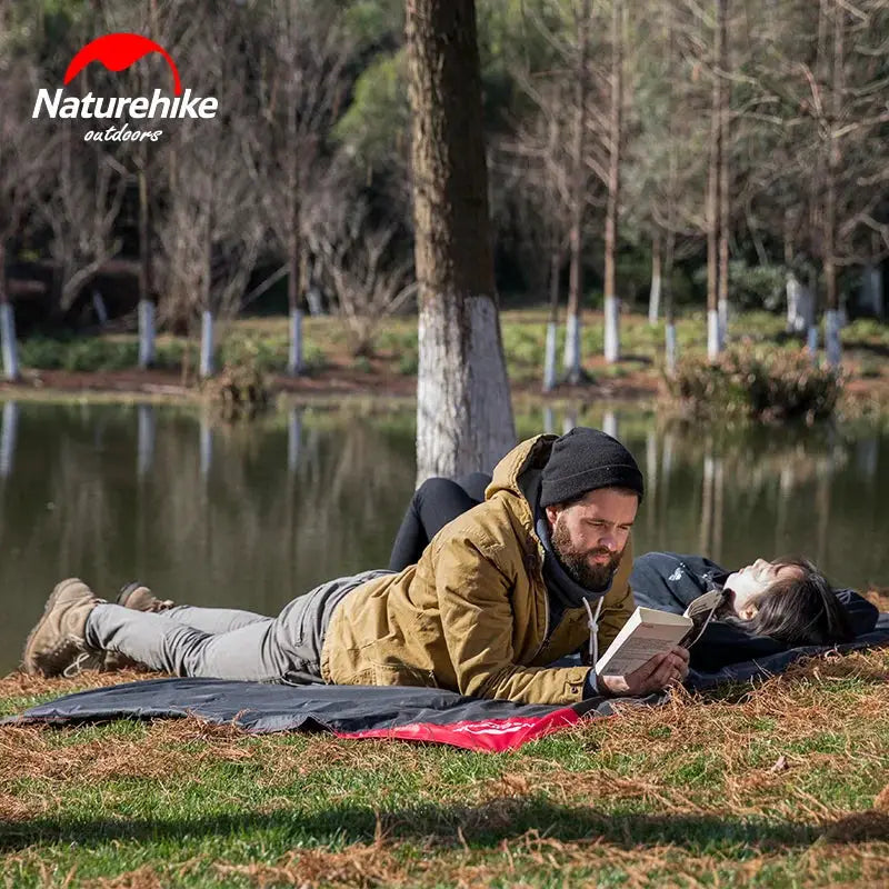 Naturehike pocket beach mat with logo visible on grass beside a pond; couple relaxing.
