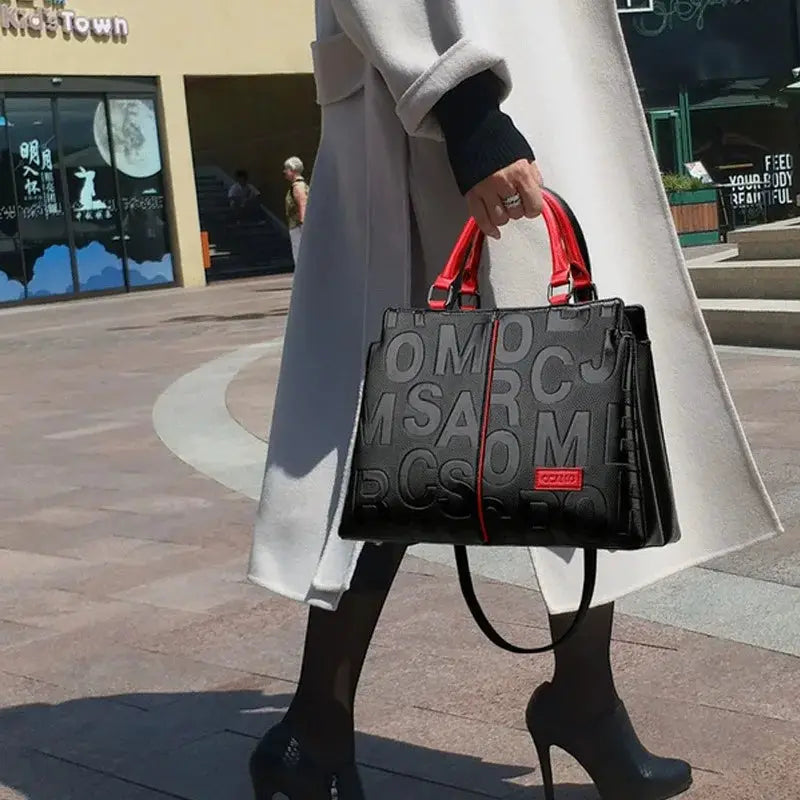 Simples Market black PU leather crossbody tote bag with embossed lettering and red top handles.