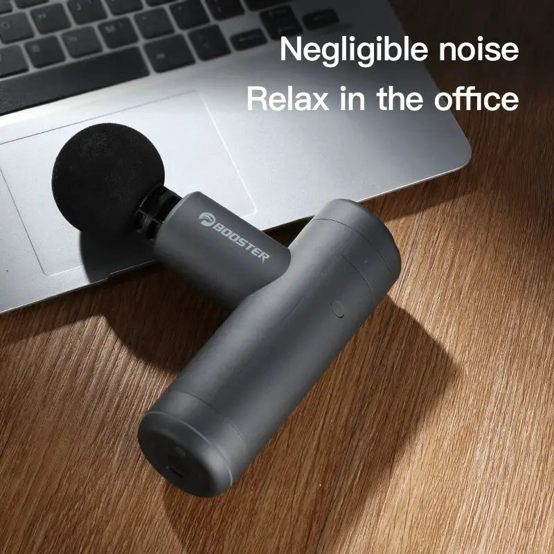 Booster Mini X massage gun back and neck massager, dark gray with foam head on wooden desk