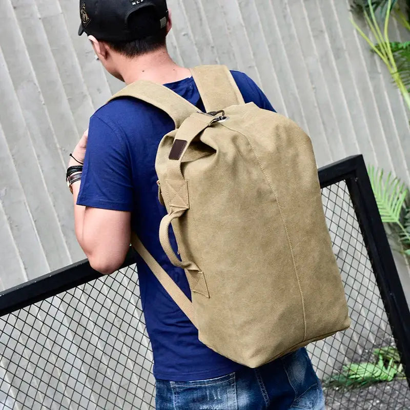 Backpack large-capacity canvas travel bag in tan, worn by a man in a blue shirt