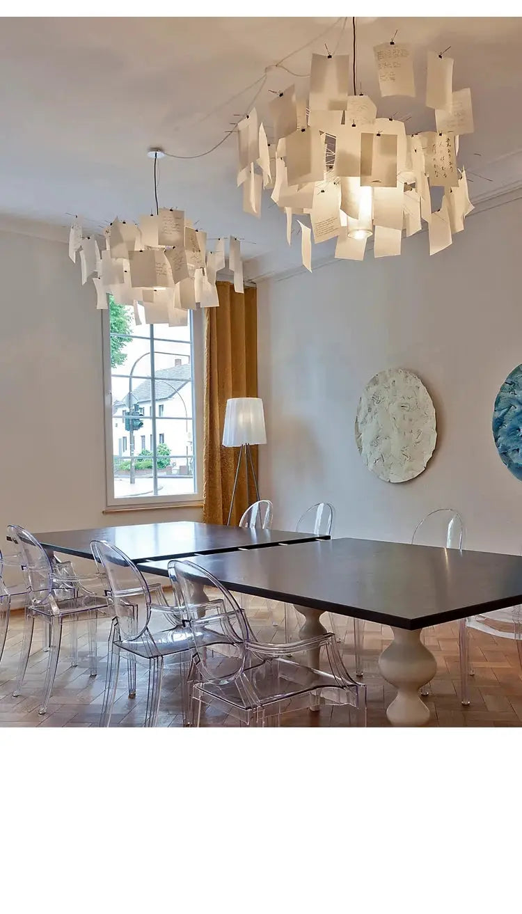 Two Ingo Maurer style paper chandeliers replica with white notes hanging from wires over a dark dining table.