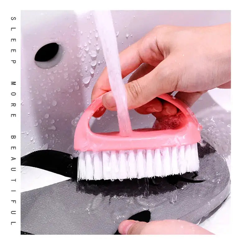 Pink egg-shaped cleaning brush with white bristles being used to scrub a wet surface under running water.