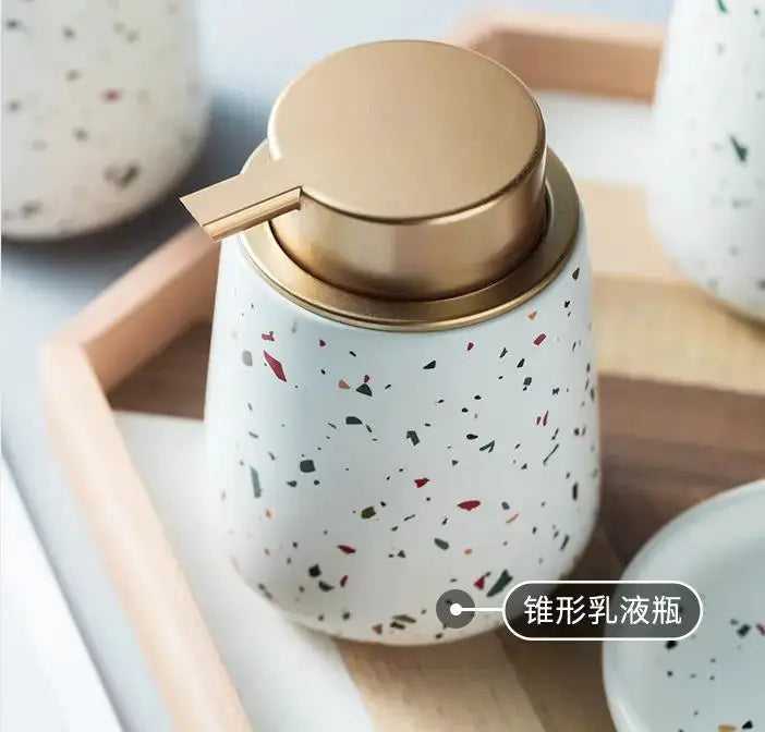Terrazzo ceramic emulsion bottle with gold pump, white speckled finish, by Simples Market on a wooden tray