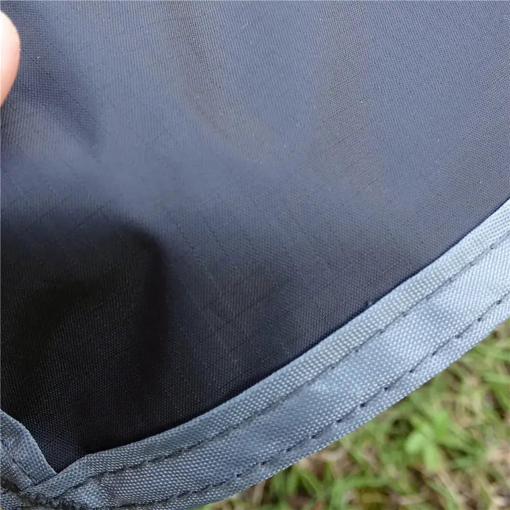 Waterproof camping mat in dark blue nylon with a stitched border, shown on grass.