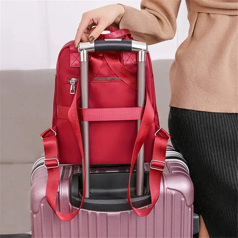 Red waterproof Oxford backpack on a pink suitcase with red shoulder straps.