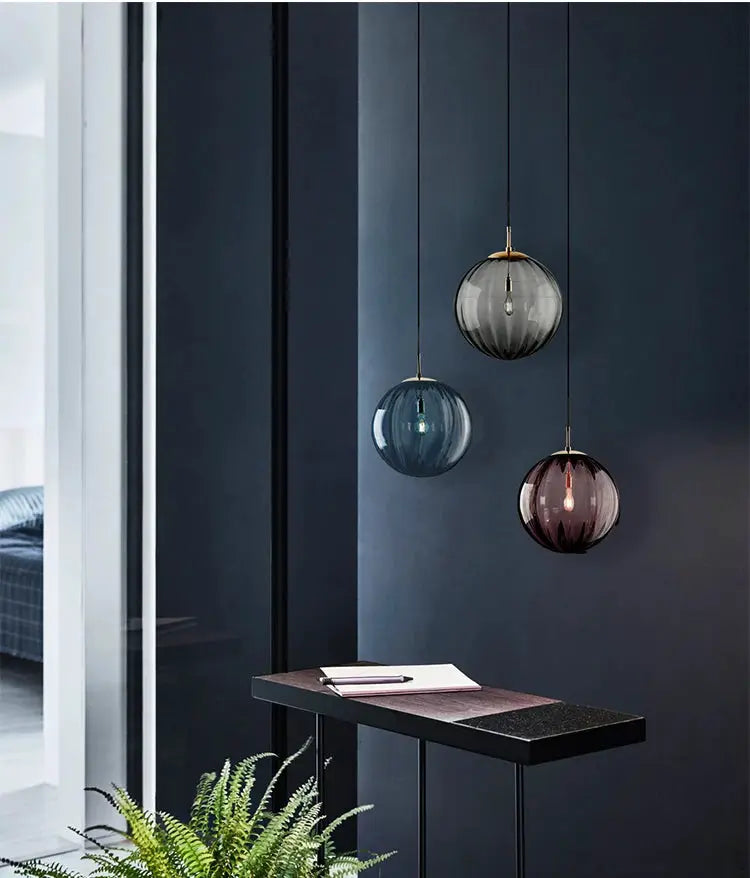 Modern LED glass ball pendant lights with three hanging spheres in gray, blue, and burgundy over a dark desk.