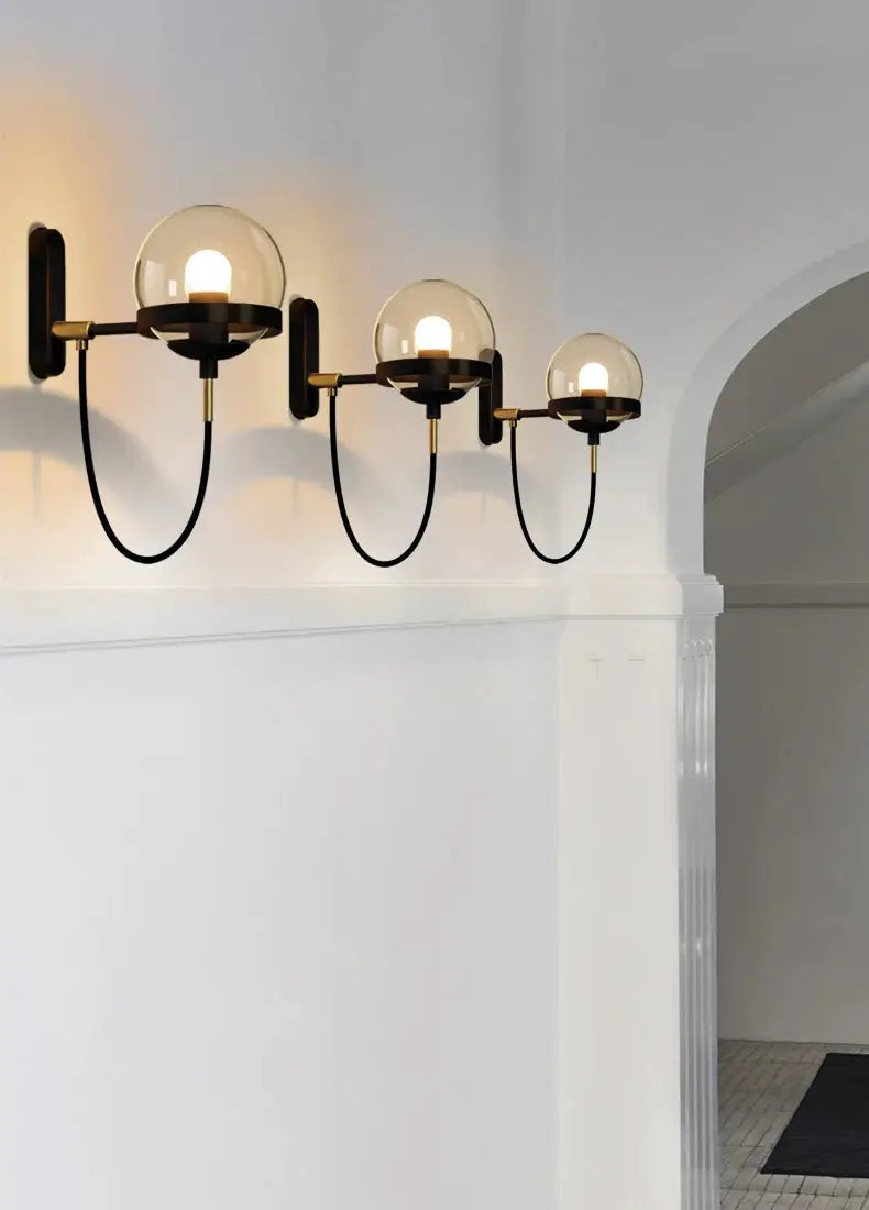 Modern glass ball wall lamp with three globes on black metal arms and brass accents, wall-mounted fixture