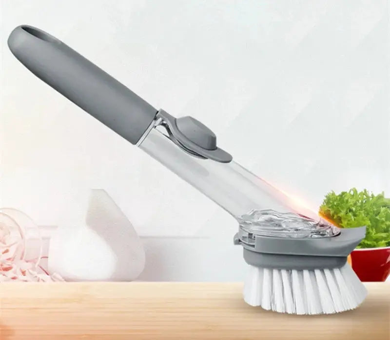 Refillable liquid cleaning brush with long gray handle and soap dispenser head, clear reservoir, white bristles.