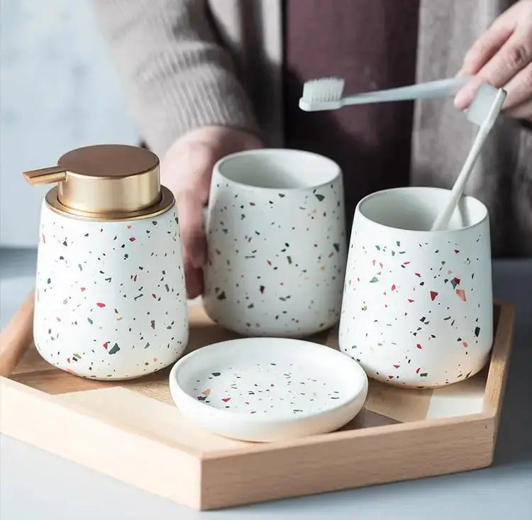Terrazzo ceramic bathroom set, four pieces: emulsion bottle, gargle cup, toothbrush holder, soap dish on a wooden tray.