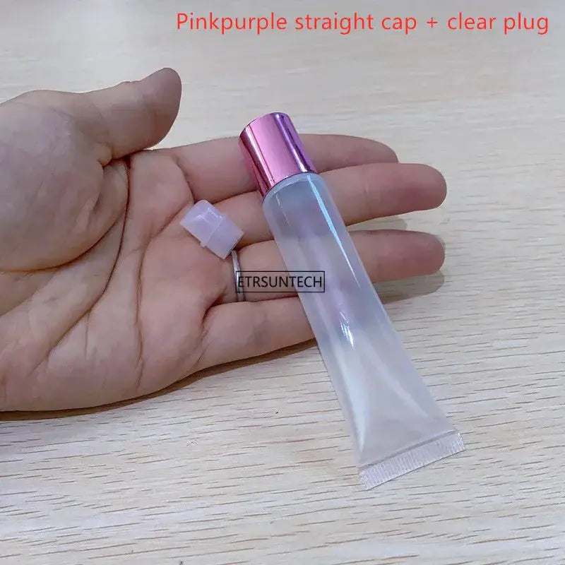 Empty clear lip gloss container with pink metallic cap; held in hand, includes white cap