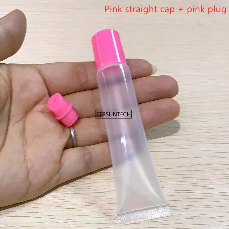 Clear empty lipstick tube with pink cap; pink plug beside hand