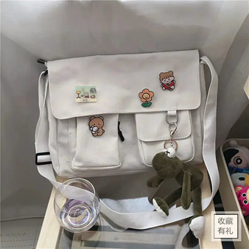 White canvas messenger bag by Simples Market with cartoon patches and plush keychain
