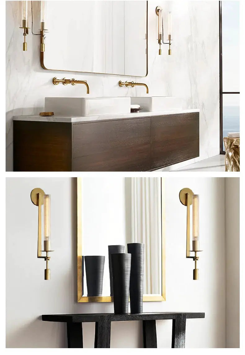Modern copper wall sconces with glass cylinders, flanking a gold-framed mirror over a marble bathroom vanity.