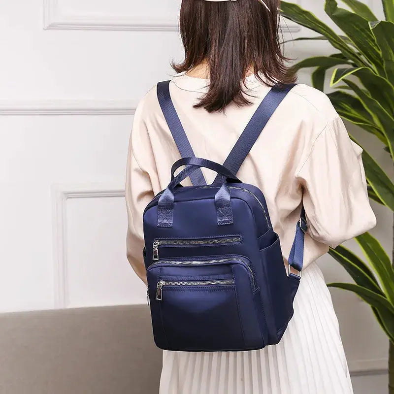 Navy blue Oxford backpack with multiple zip pockets, worn by a woman for casual travel