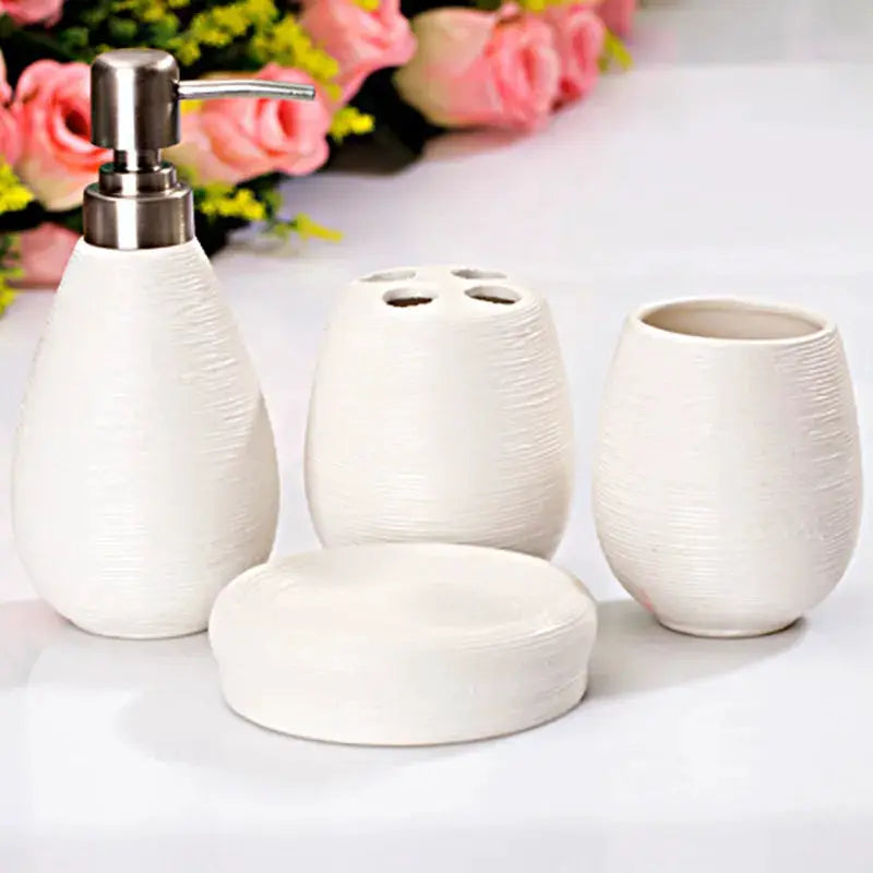 Four-piece white ceramic bathroom accessory set with pump dispenser, toothbrush holder, tumbler, and soap dish.