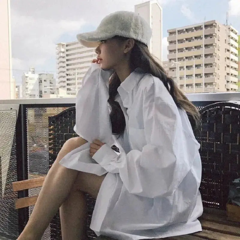 Oversize white button-up shirt worn by a woman on a balcony with city buildings in the background.