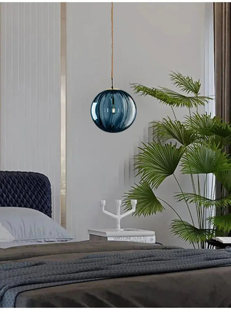 LED pendant light with blue glass globe on brown cord in a modern bedroom.