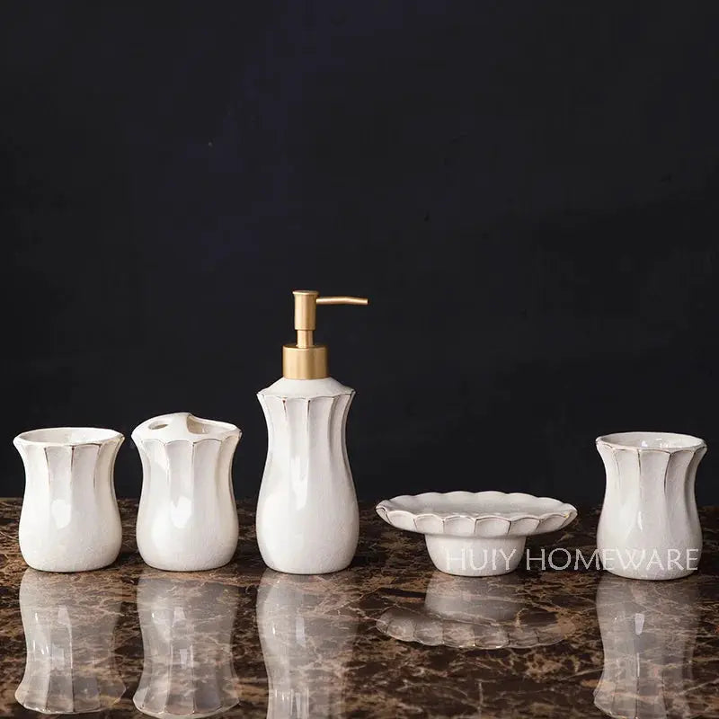 White ceramic European-style bathroom five-piece wash set with dispenser, two cups, dish, and tumbler on dark marble