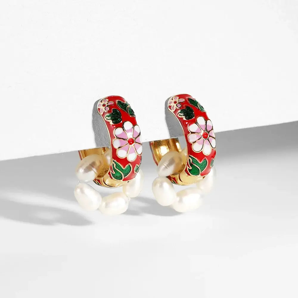 Pair of red enamel flower huggie hoop earrings with white petals, green leaves, gold-tone metal, and pearl accents