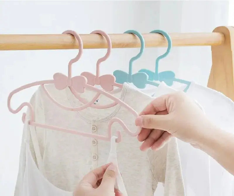 Baby clothes hangers set in pastel pink and blue plastic with bow tops on a wooden rod.