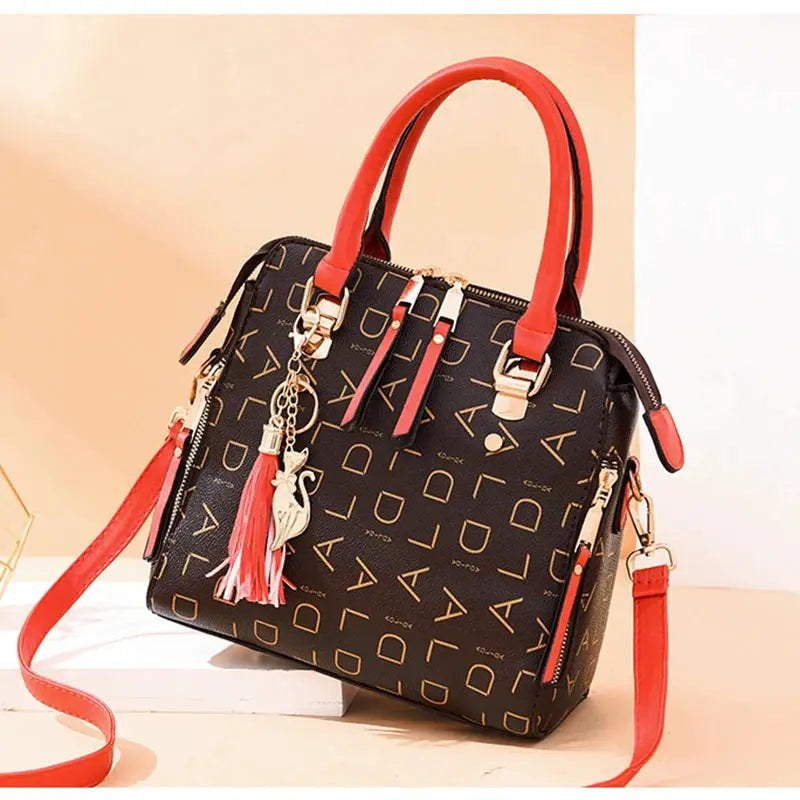 Simples Market PU leather handbag with red top handles, black body with gold letter pattern and tassel charm.