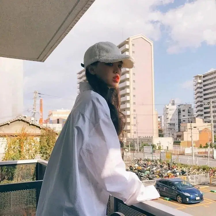 White oversized long-sleeve button-up shirt, minimalist chic casual blouse worn by model on balcony.