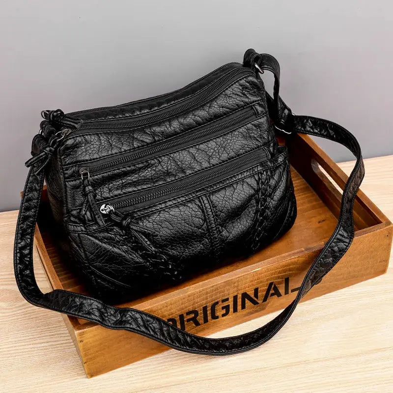 Black PU leather-look women's messenger bag with multiple zip pockets and a long crossbody strap.