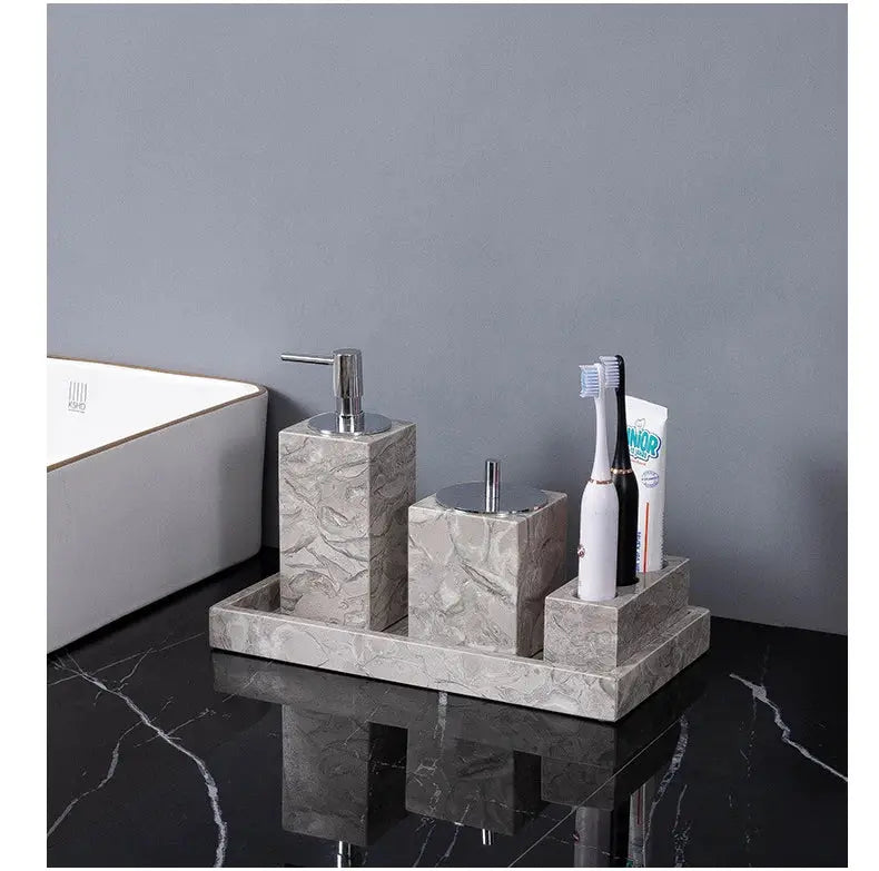Natural marble bathroom accessories set with soap dispenser, lidded jar, and toothbrush holder on a tray.