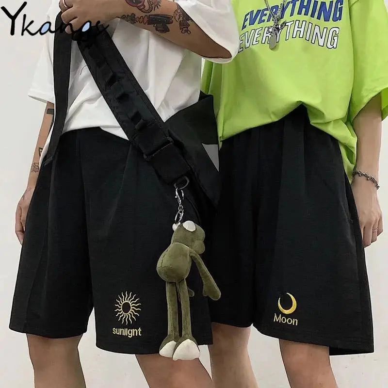 Women's black shorts (2) with sun and moon embroidery; shown with lime green tee and white tee, plush frog keychain.