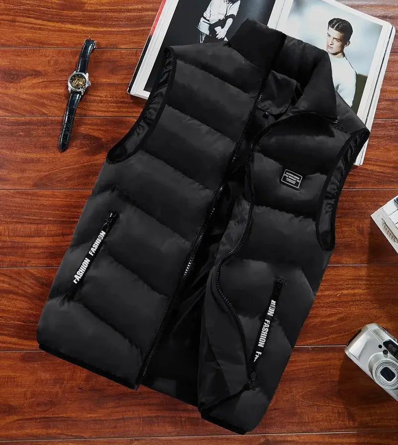 Black quilted sleeveless padded vest with front zipper and zip pockets; seen with a watch and camera on a wooden floor.