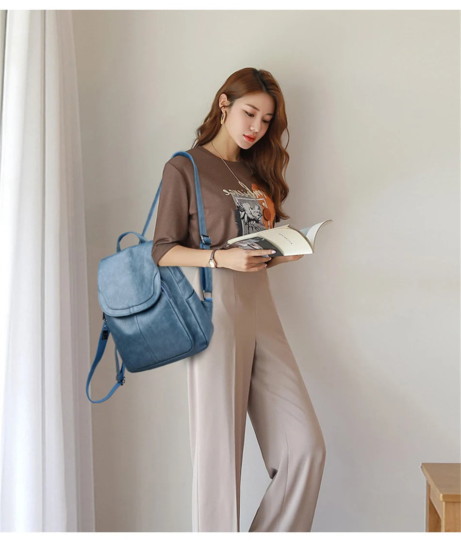 Genuine Women Soft Leather Backpack in blue by Simples Market; worn by a woman in a brown top while reading a book