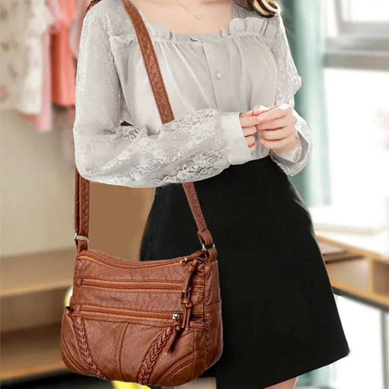 Women's messenger bag in brown PU leather with braided strap and multiple zip pockets.