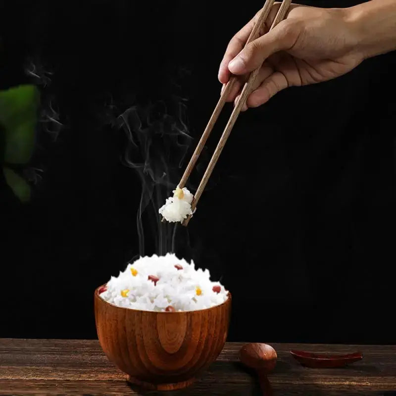 Wooden rosewood chopsticks lifting rice from a wooden bowl; reusable kitchen utensils