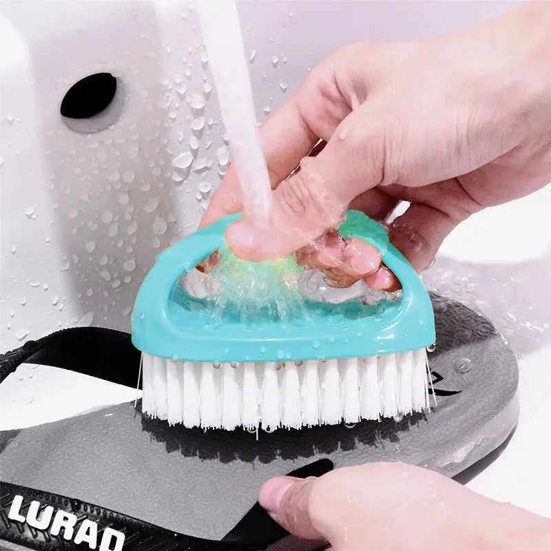 Egg-shaped turquoise cleaning brush with white bristles scrubbing a shoe under running water.