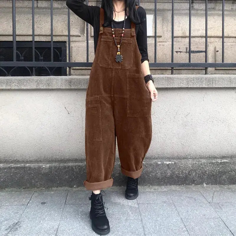 Brown corduroy overalls jumpsuit, oversized bib suspender style with rolled cuffs, paired with black boots.
