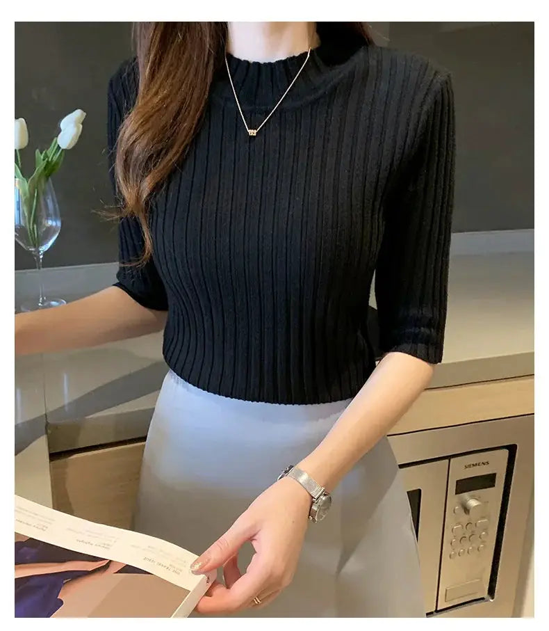Simples Market black ribbed knit short-sleeve women's blouse with a light gray skirt; necklace and wristwatch visible.