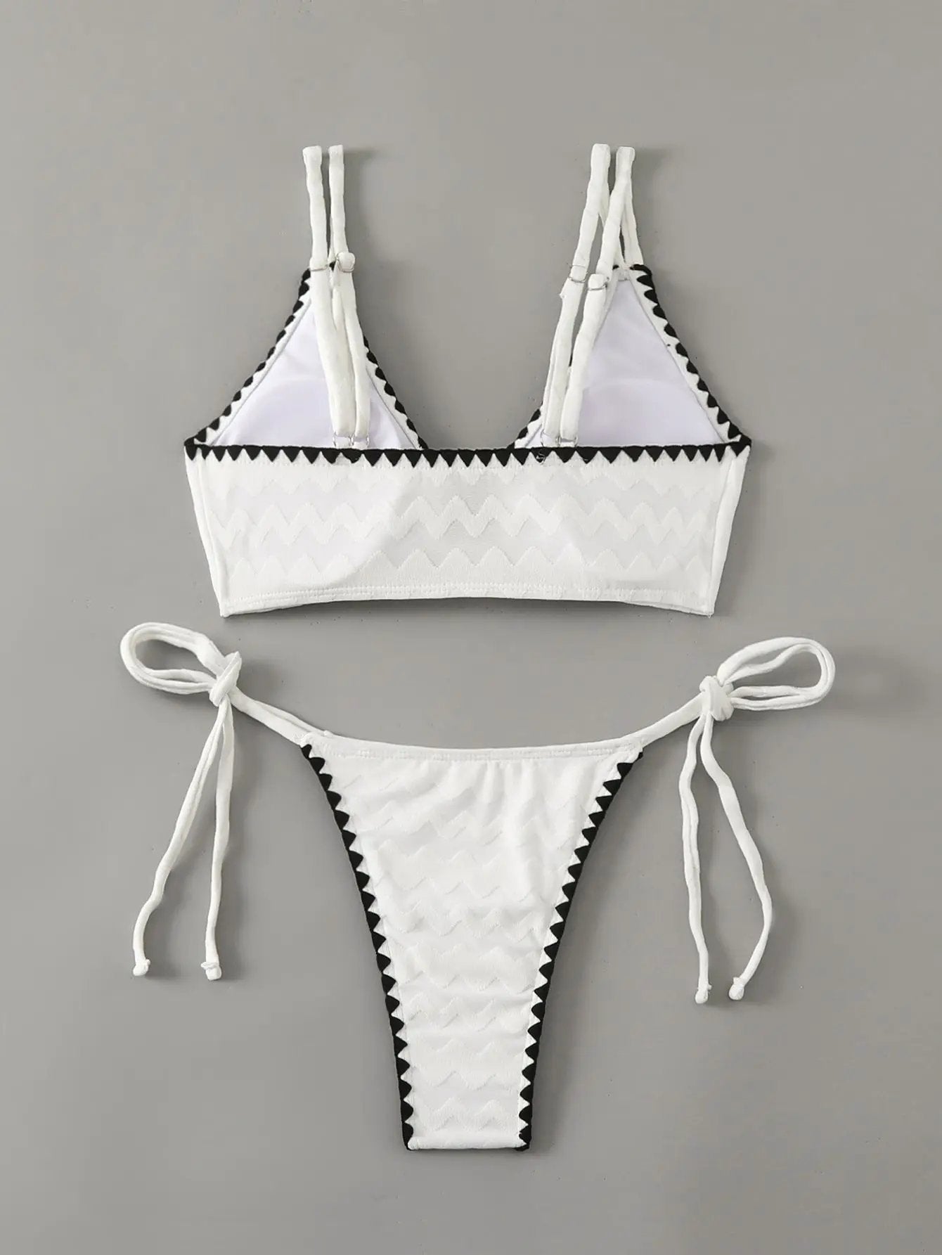 White two-piece bikini with black zigzag trim; triangle top with double straps and tie sides, high-cut bottoms