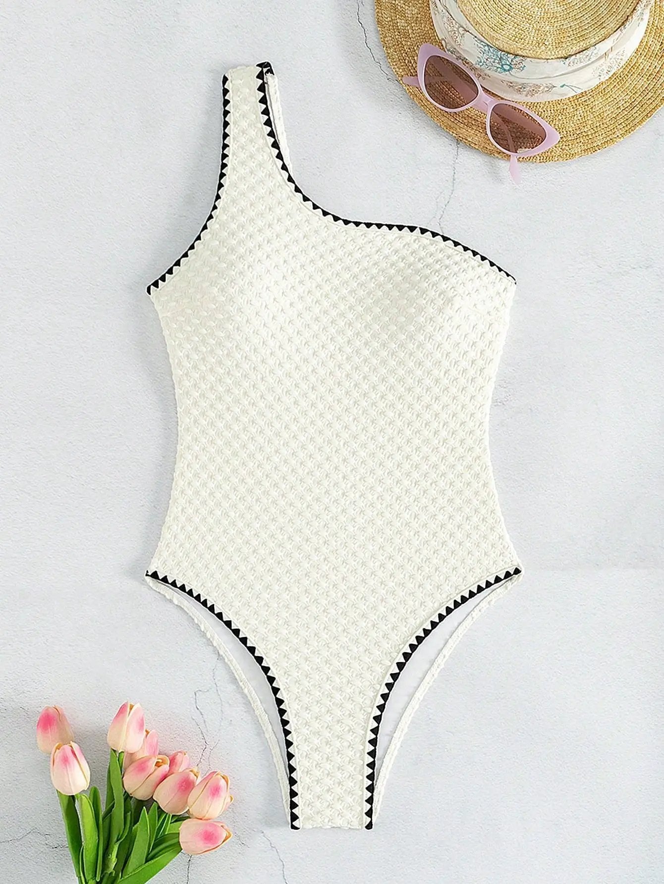 One-piece white textured swimsuit with a single shoulder strap, black zigzag trim, high-cut legs