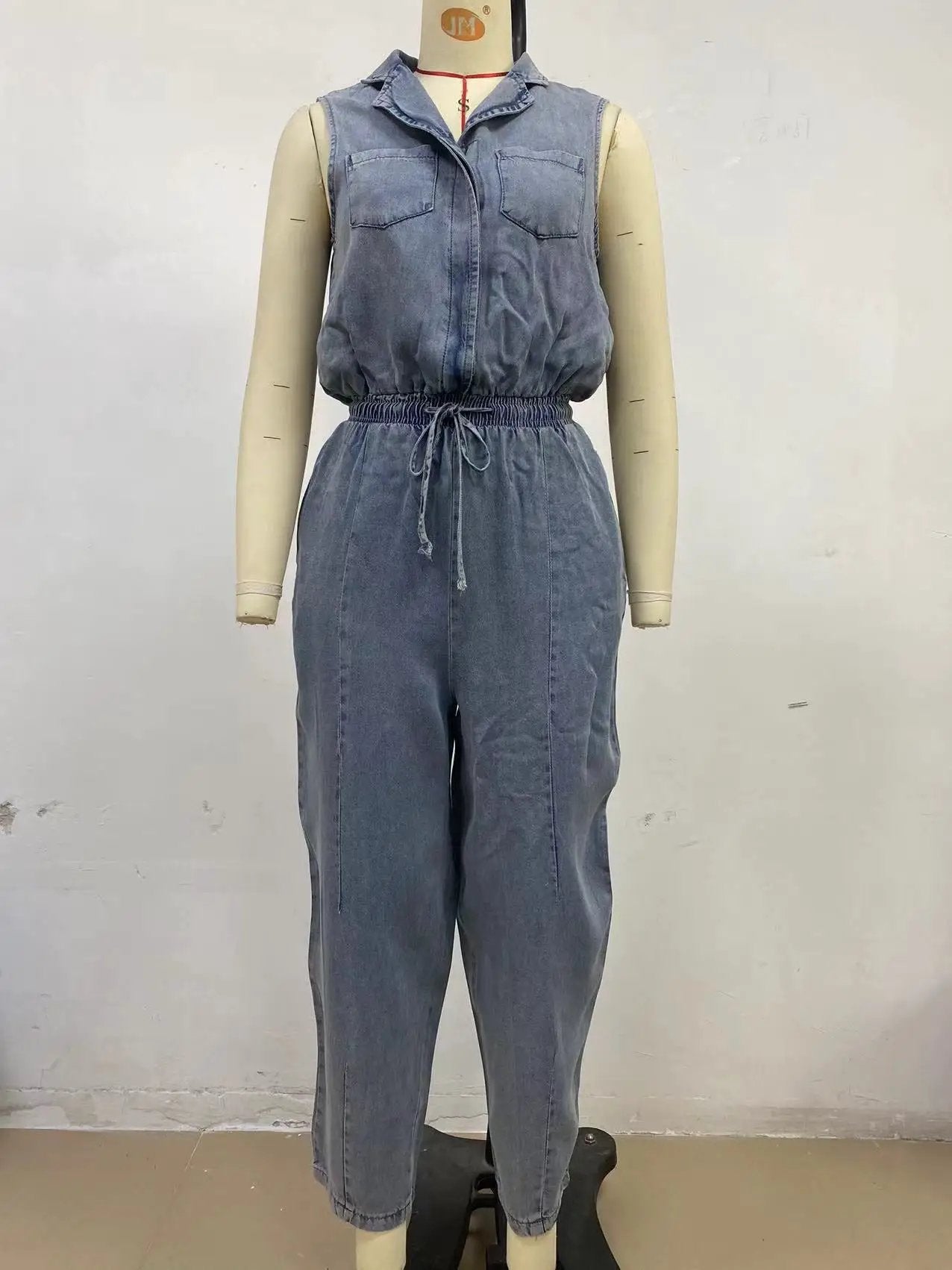 Women's sleeveless denim jumpsuit with front pockets and drawstring waist in blue denim.
