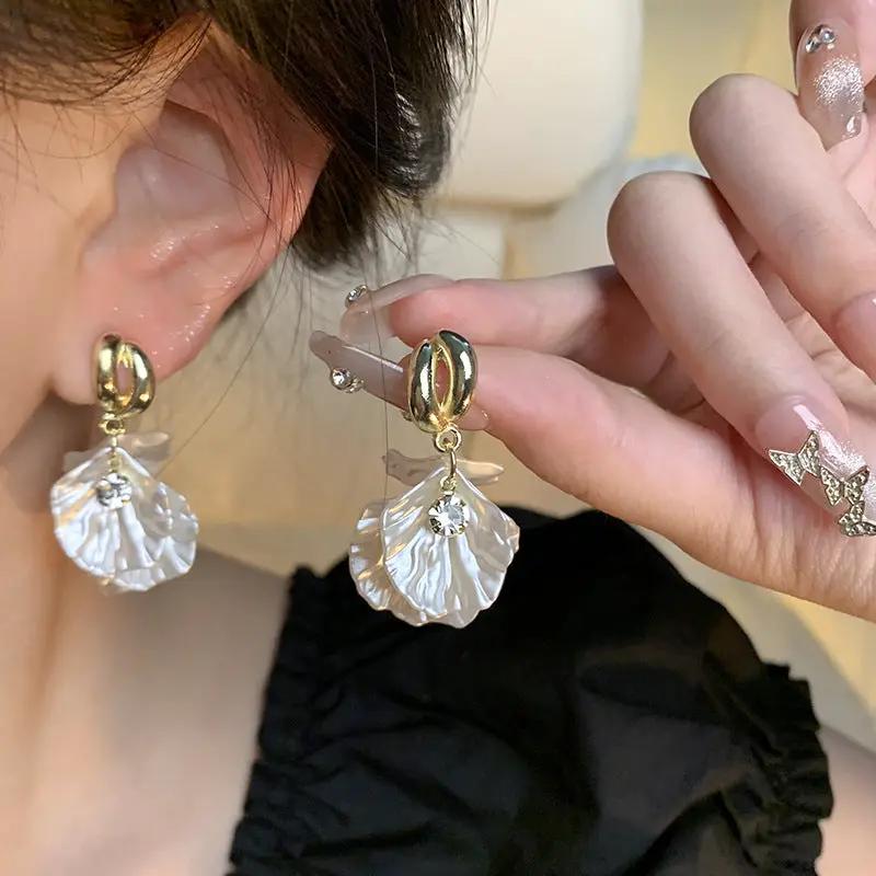 Simples Market glossy shell flower pendant earrings, pair of gold hoops with clear shell petals and rhinestone accents.