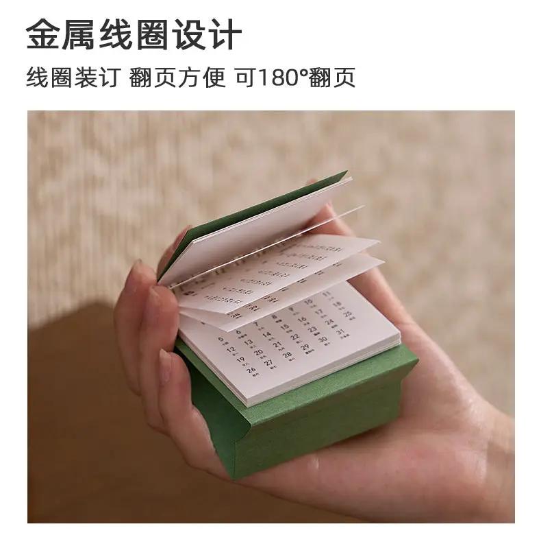 Mini desk calendar with metal coil binding in a green box by Simples Market