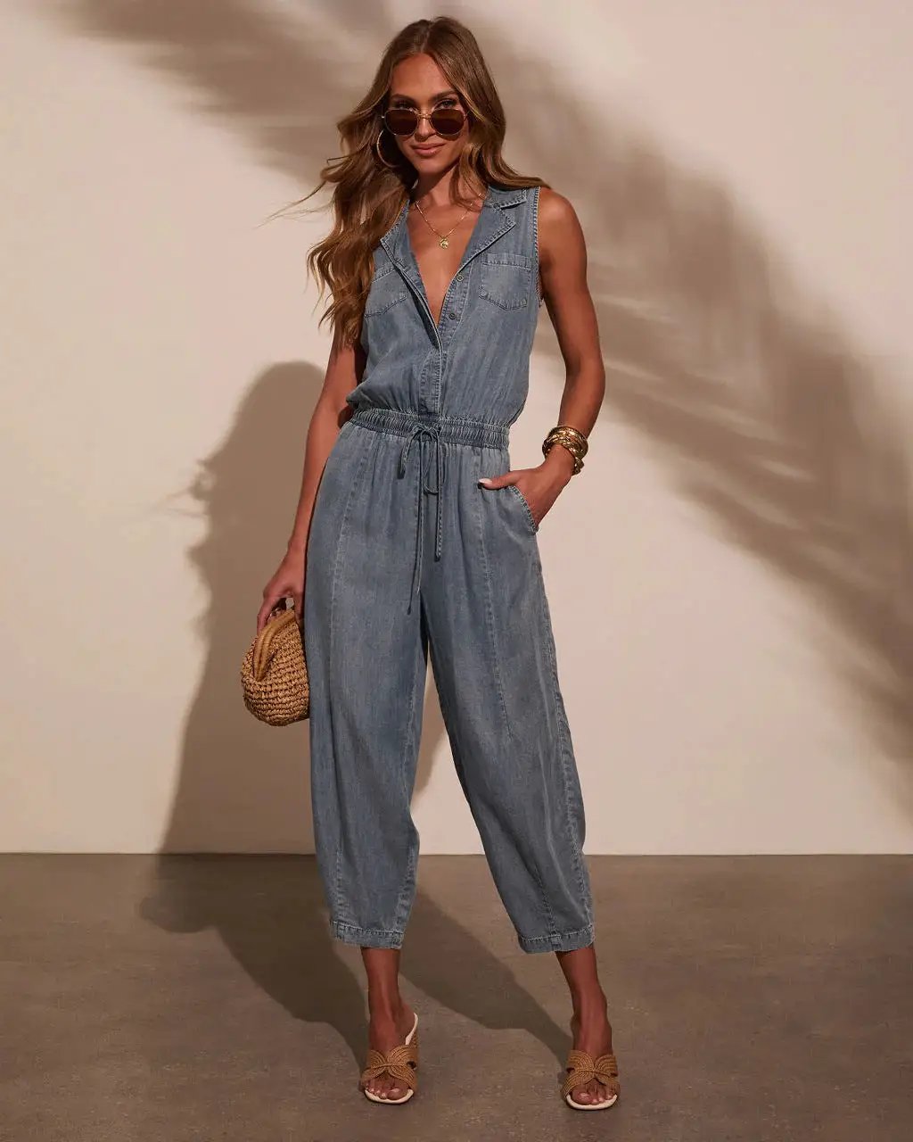 Women's sleeveless denim jumpsuit with drawstring waist, front pockets, casual one-piece.