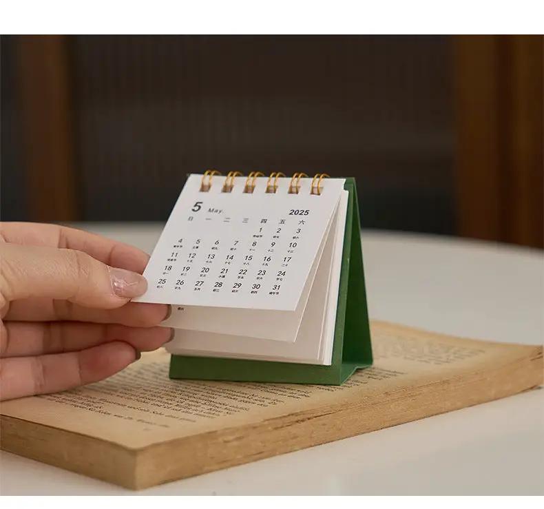 2026 mini desk calendar by Simples Market, green triangular stand with white coil-bound pages.