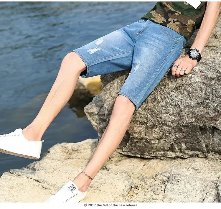 Men's light blue distressed denim shorts, knee-length with ripped patches, casual summer wear.