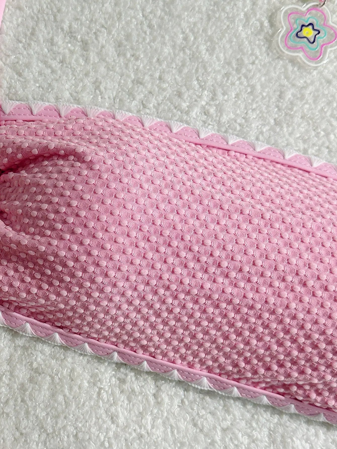 Pink textured bikini fabric close-up with small raised dots and white scalloped edge