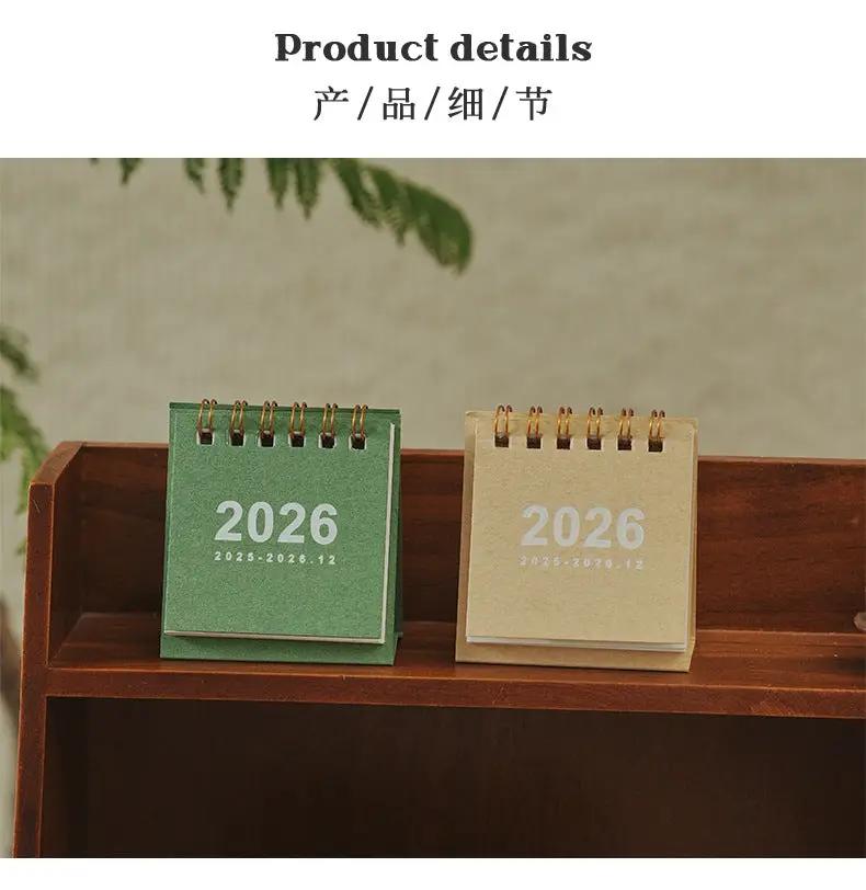Two mini desk calendars with coil bindings, green and kraft beige, 2026, on a wooden shelf.