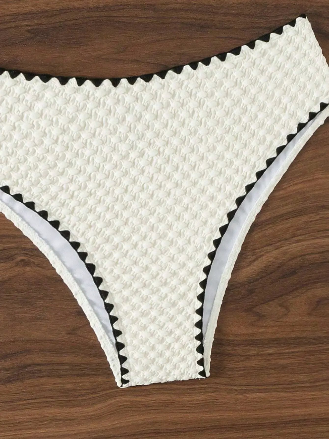 Bikini bottom in white textured fabric with black zigzag trim and light blue edging.