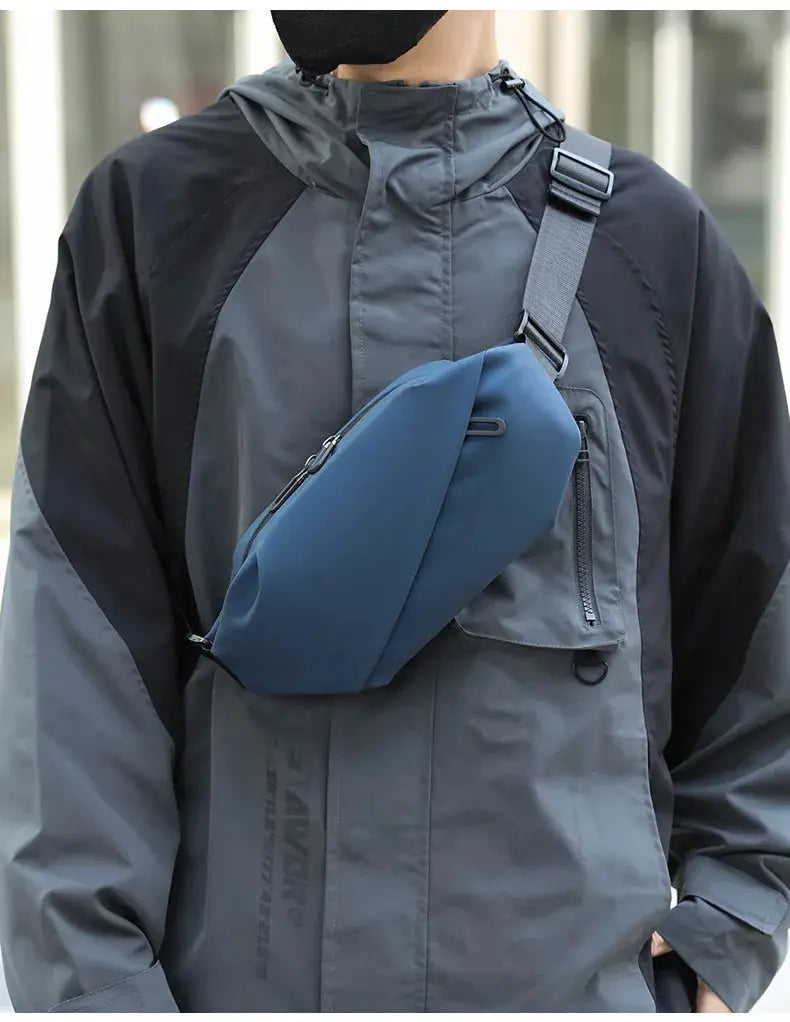 Waist bag by Simples Market in blue, worn across the chest over a gray outdoor jacket.