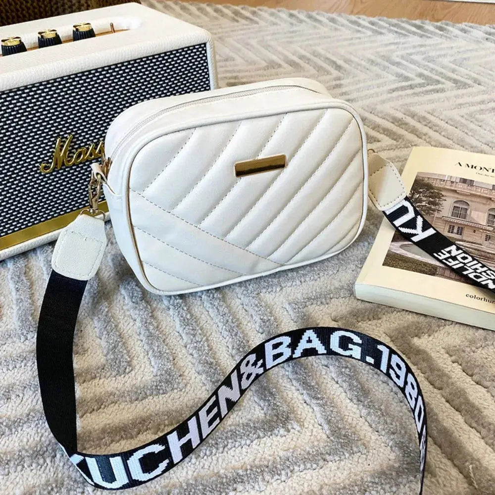 White quilted PU shoulder bag with diagonal stitching, gold plaque, and a black strap with white branding